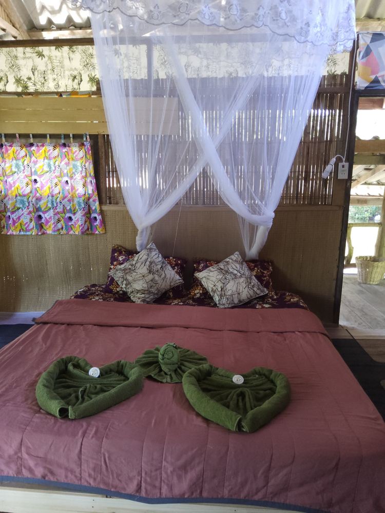 Bed with rose-coloured cover and bright curtains